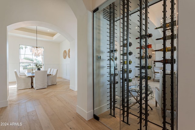 wine area featuring a raised ceiling, light hardwood / wood-style flooring, and an inviting chandelier