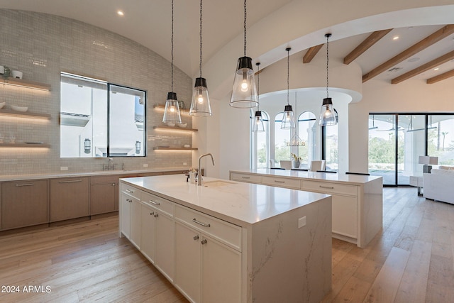 kitchen featuring a center island with sink, sink, white cabinets, and backsplash