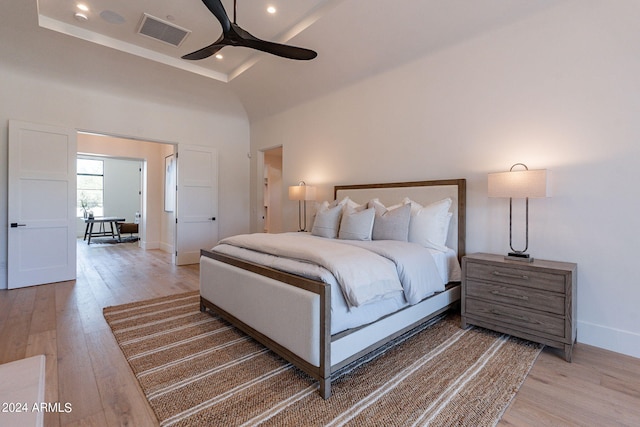 bedroom with a high ceiling, hardwood / wood-style flooring, a raised ceiling, and ceiling fan