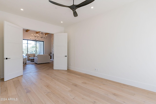 unfurnished room featuring ceiling fan with notable chandelier and light wood-type flooring