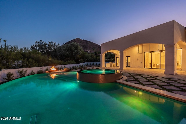 pool at dusk featuring a mountain view, an in ground hot tub, and a patio