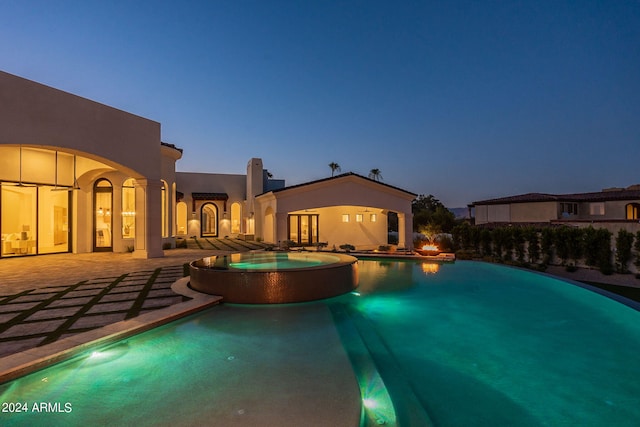 pool at dusk featuring a patio area and an in ground hot tub