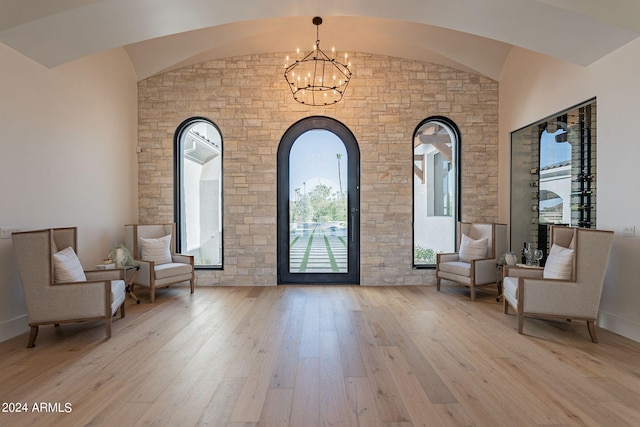 living area featuring a notable chandelier, vaulted ceiling, and light hardwood / wood-style flooring