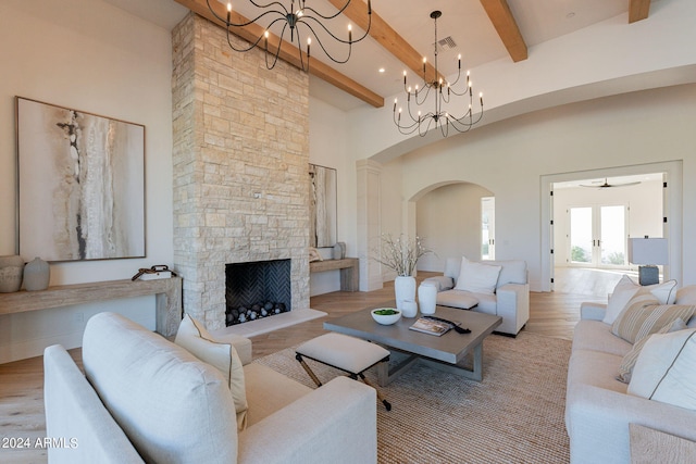 living room with french doors, a towering ceiling, beam ceiling, light hardwood / wood-style flooring, and a stone fireplace