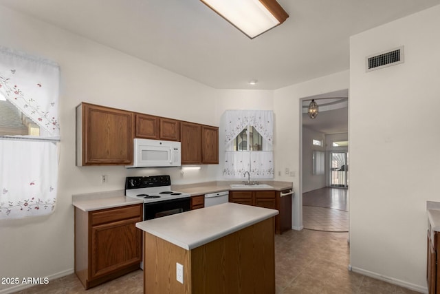 kitchen with light countertops, visible vents, white appliances, a sink, and a center island