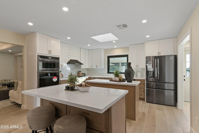 kitchen with a skylight, a center island, stainless steel appliances, a breakfast bar area, and white cabinets