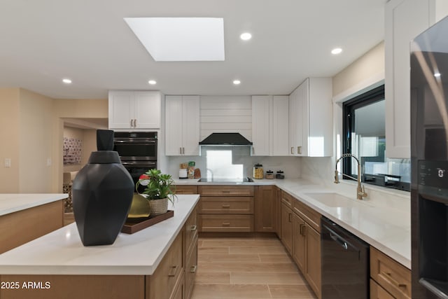 kitchen featuring a skylight, white cabinetry, sink, a center island, and black appliances