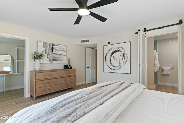 bedroom featuring ceiling fan, a barn door, and connected bathroom