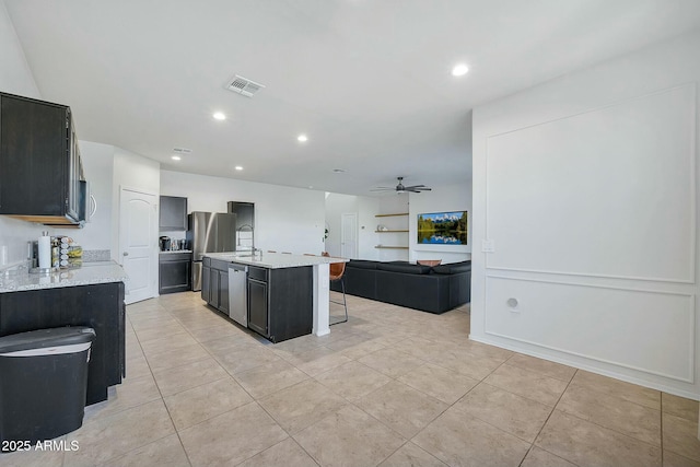 kitchen featuring ceiling fan, appliances with stainless steel finishes, light stone countertops, and an island with sink