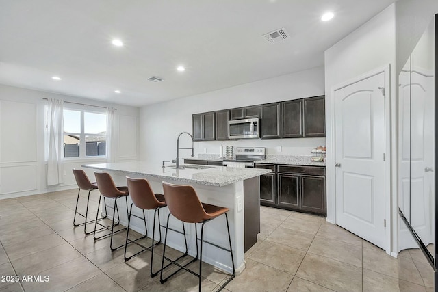 kitchen featuring appliances with stainless steel finishes, a breakfast bar, sink, light tile patterned floors, and a center island with sink