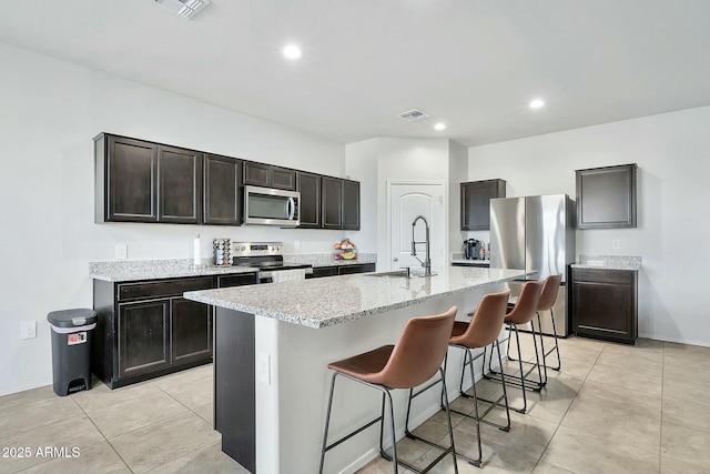 kitchen with appliances with stainless steel finishes, sink, a breakfast bar area, dark brown cabinetry, and a center island with sink