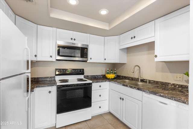 kitchen featuring white appliances, light tile patterned floors, white cabinets, a raised ceiling, and a sink