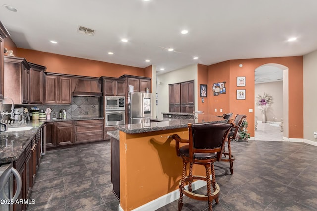 kitchen featuring visible vents, a center island, arched walkways, appliances with stainless steel finishes, and decorative backsplash