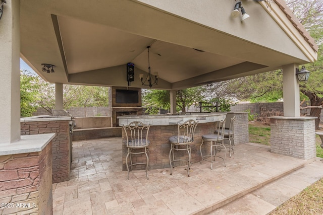 view of patio with outdoor dry bar, an outdoor stone fireplace, a gazebo, and fence