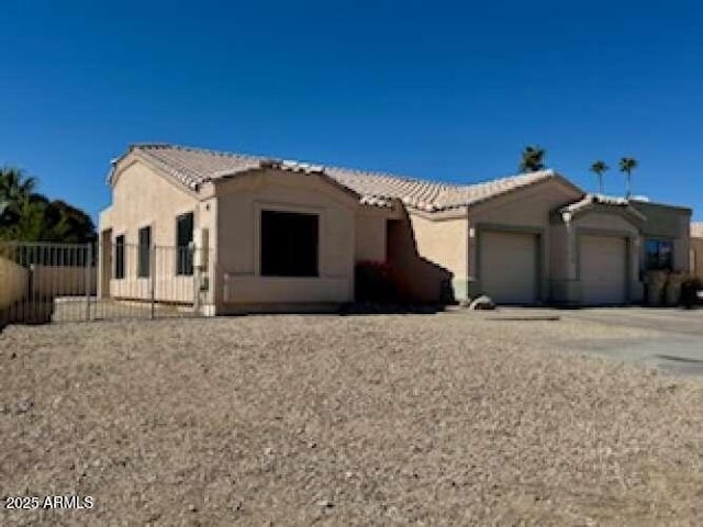 view of front of house featuring fence, a tiled roof, an attached garage, and stucco siding