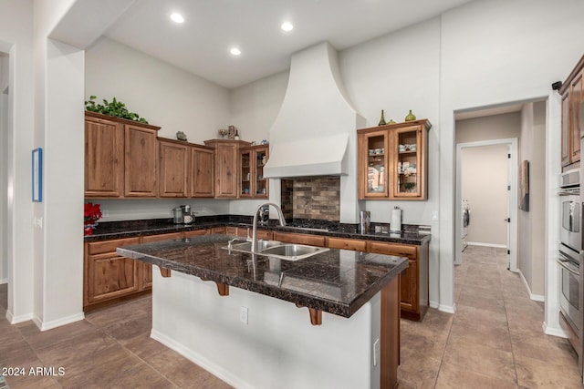 kitchen with a kitchen bar, a center island with sink, custom range hood, and sink