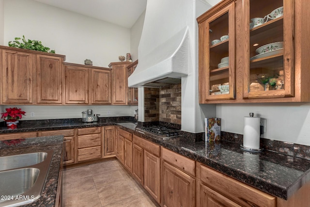 kitchen with stainless steel gas stovetop, custom exhaust hood, dark stone counters, sink, and decorative backsplash