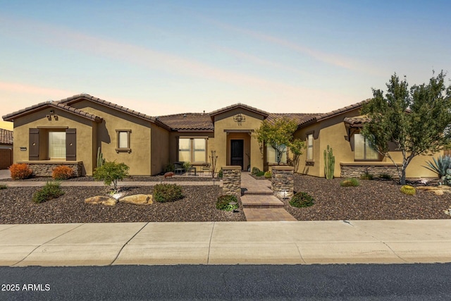 mediterranean / spanish house featuring stucco siding, a tile roof, and stone siding