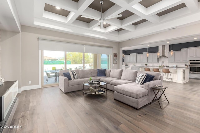 living area with a high ceiling, coffered ceiling, ceiling fan, and wood finished floors