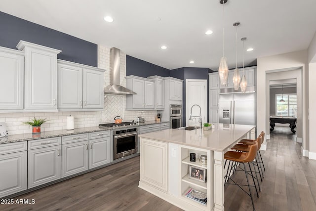 kitchen featuring a sink, backsplash, wall chimney range hood, and dark wood-type flooring