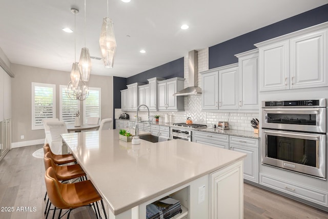 kitchen featuring stainless steel appliances, a chandelier, decorative backsplash, a sink, and wall chimney exhaust hood