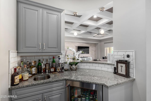 bar with coffered ceiling, wine cooler, a sink, backsplash, and indoor wet bar