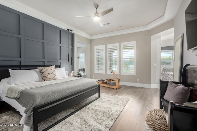 bedroom with visible vents, a decorative wall, light wood-style flooring, and ceiling fan