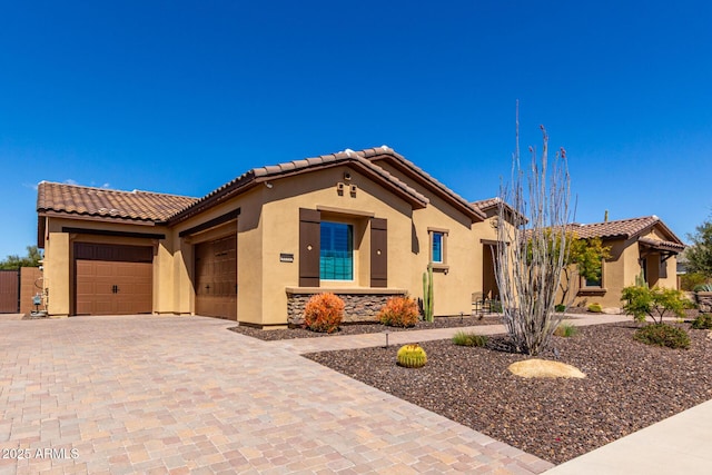 mediterranean / spanish-style home with a tiled roof, a garage, decorative driveway, and stucco siding