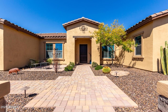 view of exterior entry featuring stucco siding, a tiled roof, and a patio