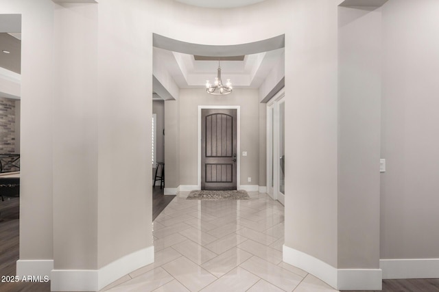 entryway featuring a tray ceiling, baseboards, and a notable chandelier