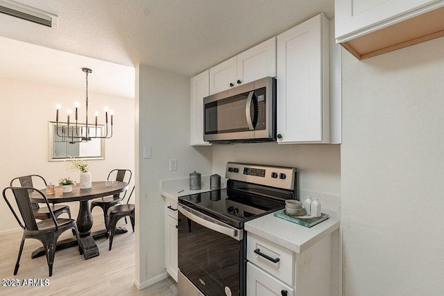 4268 N 68th Ave, Phoenix, AZ 85033 - kitchen with stainless steel appliances, light countertops, a chandelier, white cabinetry, and light wood finished floors