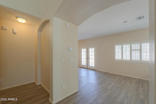 empty room featuring baseboards, visible vents, arched walkways, and wood finished floors