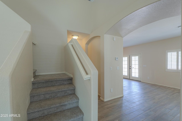 stairway with baseboards, arched walkways, wood finished floors, and french doors