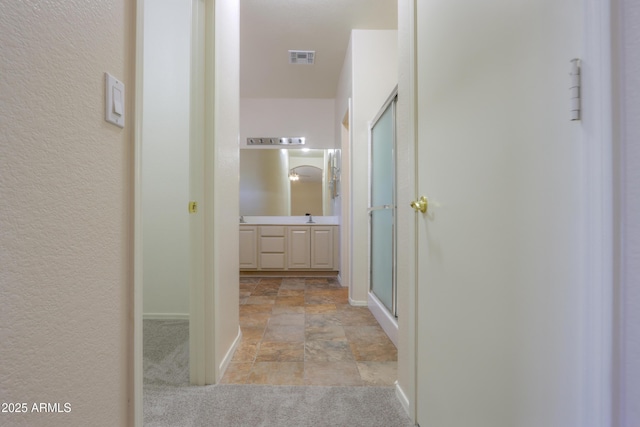 bathroom with a shower with shower door, visible vents, vanity, baseboards, and stone finish floor