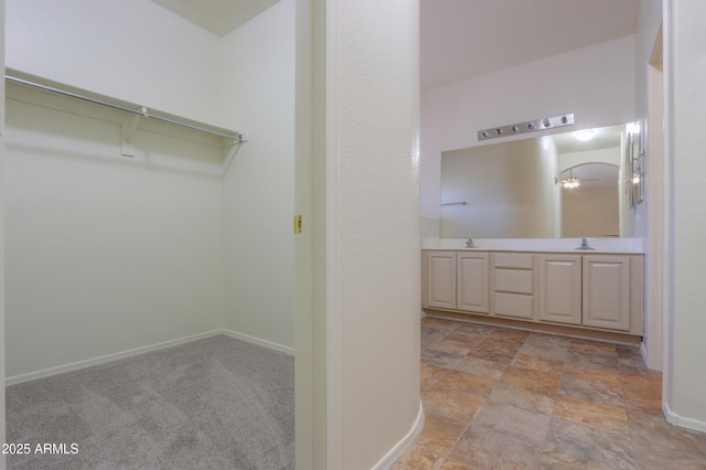 full bath with double vanity, baseboards, a walk in closet, and a sink