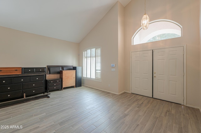 entryway with a notable chandelier, high vaulted ceiling, light wood-style flooring, and baseboards