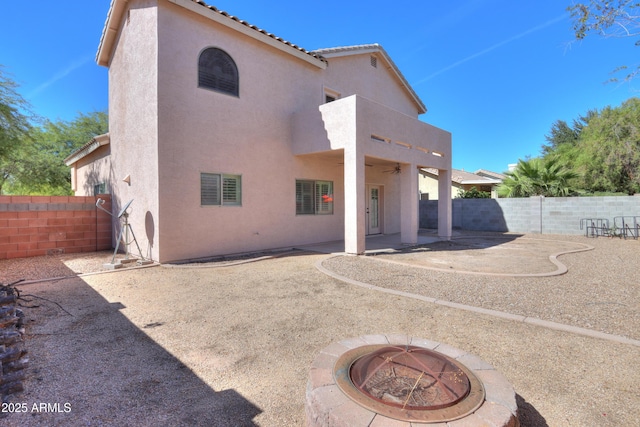 rear view of property featuring a fire pit, a patio, a fenced backyard, a tiled roof, and stucco siding