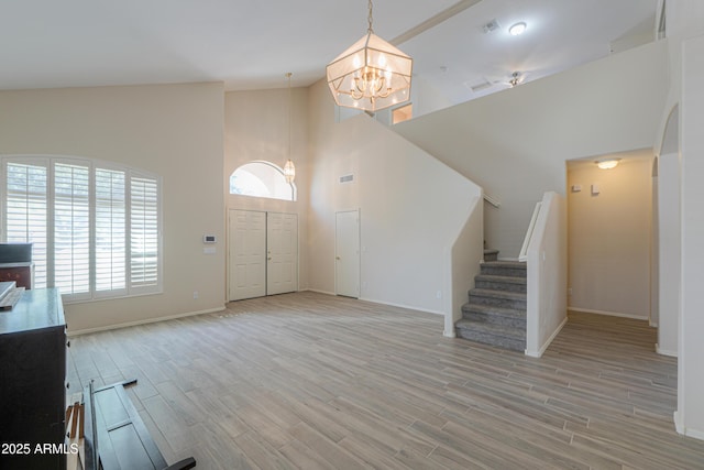 entryway featuring baseboards, a chandelier, stairway, light wood-type flooring, and high vaulted ceiling