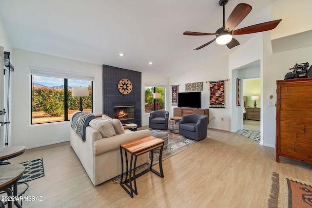 living room with a tiled fireplace, vaulted ceiling, light wood-style flooring, and baseboards