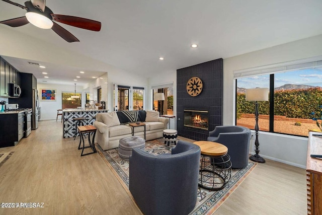 living area featuring baseboards, light wood finished floors, vaulted ceiling, a fireplace, and a ceiling fan