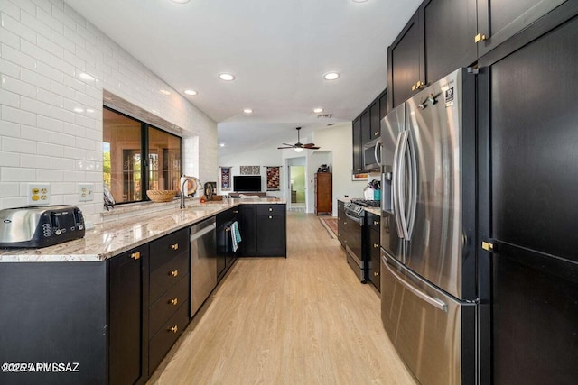kitchen with light stone countertops, dark cabinets, appliances with stainless steel finishes, light wood-type flooring, and a peninsula