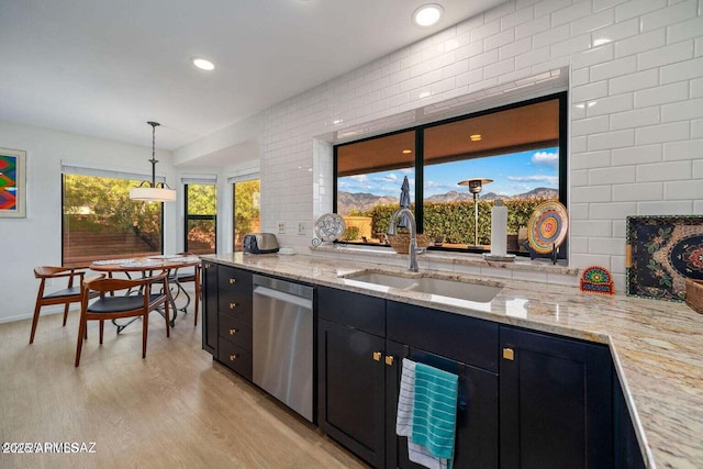 kitchen with light stone countertops, a sink, light wood-style flooring, dishwasher, and dark cabinets
