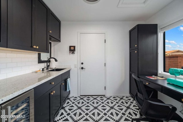 interior space with wine cooler, a sink, dark cabinets, and tasteful backsplash