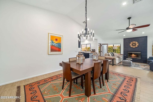 dining room featuring visible vents, vaulted ceiling, a fireplace, wood finished floors, and ceiling fan with notable chandelier