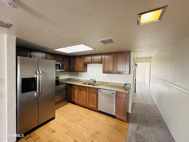 kitchen featuring light stone countertops, sink, stainless steel appliances, and light hardwood / wood-style flooring