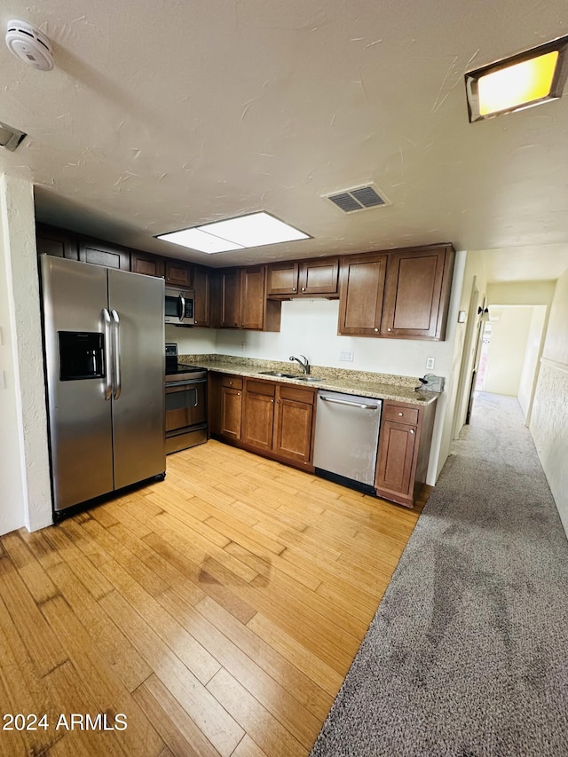 kitchen with light stone countertops, light wood-type flooring, stainless steel appliances, and sink