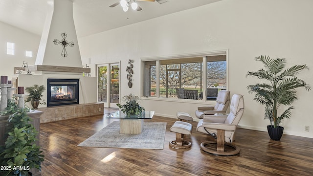 sitting room featuring baseboards, a ceiling fan, a tile fireplace, dark wood-type flooring, and high vaulted ceiling