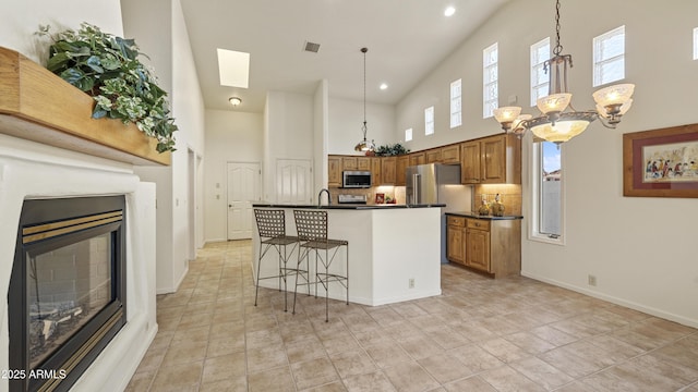 kitchen featuring brown cabinets, dark countertops, appliances with stainless steel finishes, a glass covered fireplace, and an island with sink