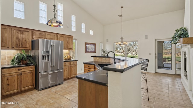 kitchen featuring high end refrigerator, dark countertops, an island with sink, brown cabinets, and a sink