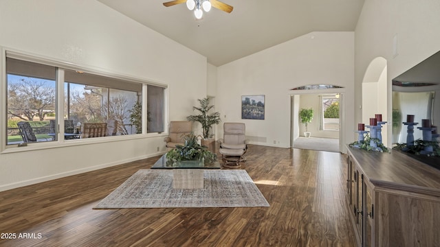 living area featuring dark wood-style floors, ceiling fan, high vaulted ceiling, and baseboards